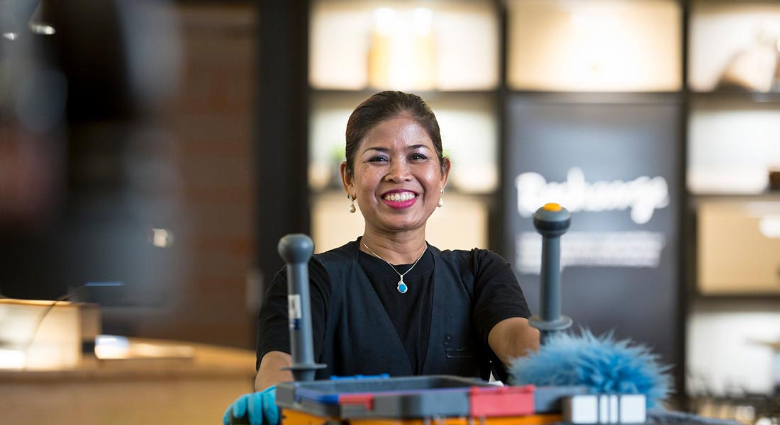 Kvindelig Coor rengøringsmedarbejder der smiler og skuber en rengøringsvogn